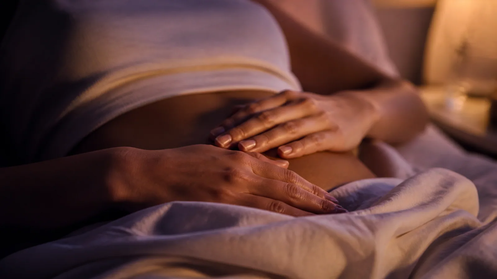 Mains posées doucement sur le ventre d'une personne allongée pour auto-traitement Reiki Shamballa avant le coucher, lumière tamisée du soir