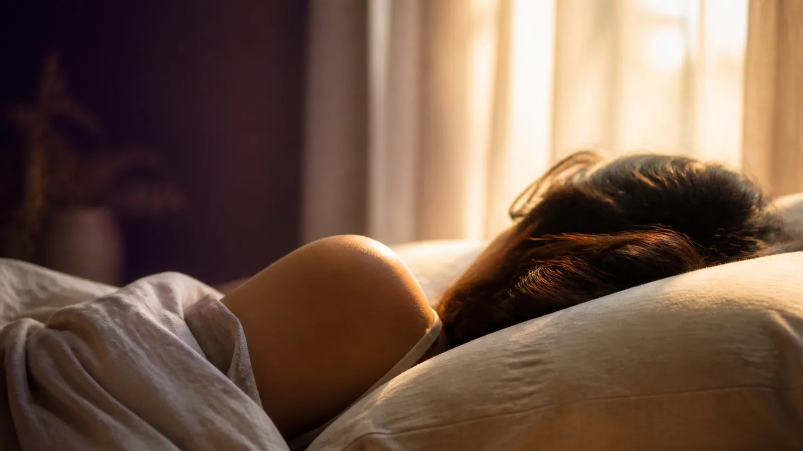 Personne endormie paisiblement avec lumière dorée matinale traversant des rideaux légers, métaphore d'un sommeil amélioré par le Reiki Shamballa